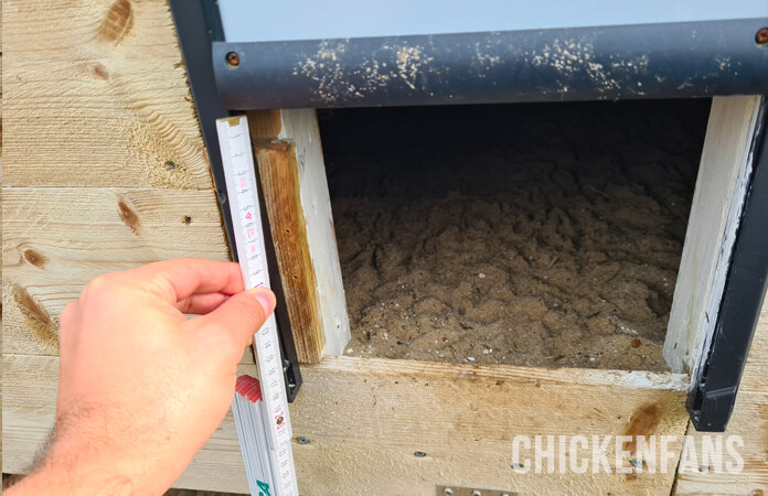 Chickenguard chicken coop door height measurement, holding a ruler in front of the entrance of the installed door