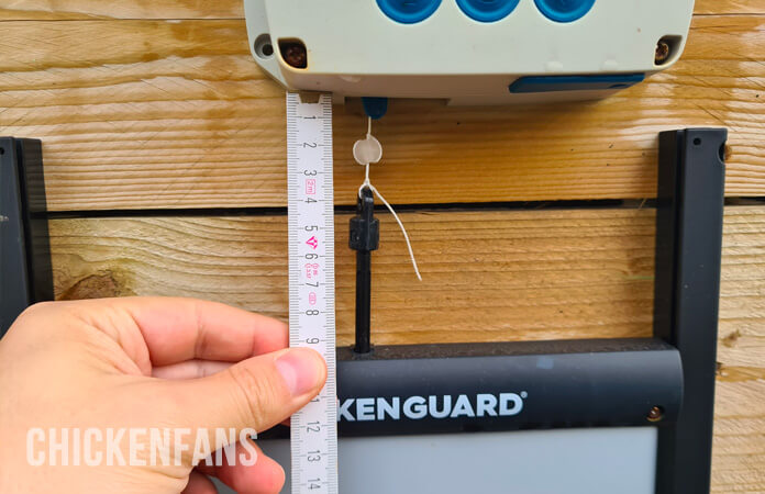 Chickenguard chicken coop door measurement of the space on top of the door, for the locking bead and cord ending, holding a ruler