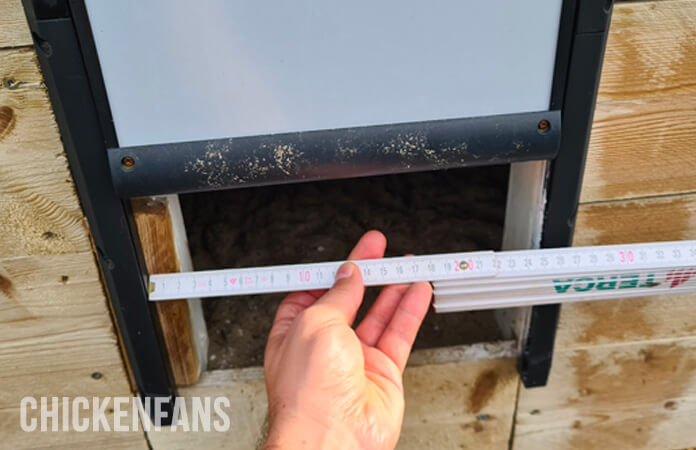 Chickenguard chicken coop door width measurement, holding a ruler in front of the entrance
